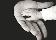 The hand of an infant reaches out to hold the hand of an older person.